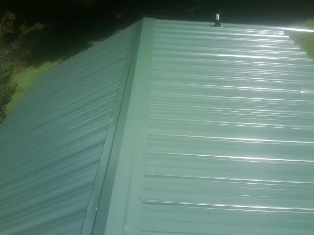 New green metal panels meeting at the ridge of a roof — Flat Roof Repair work by our crew in New Bloomfield