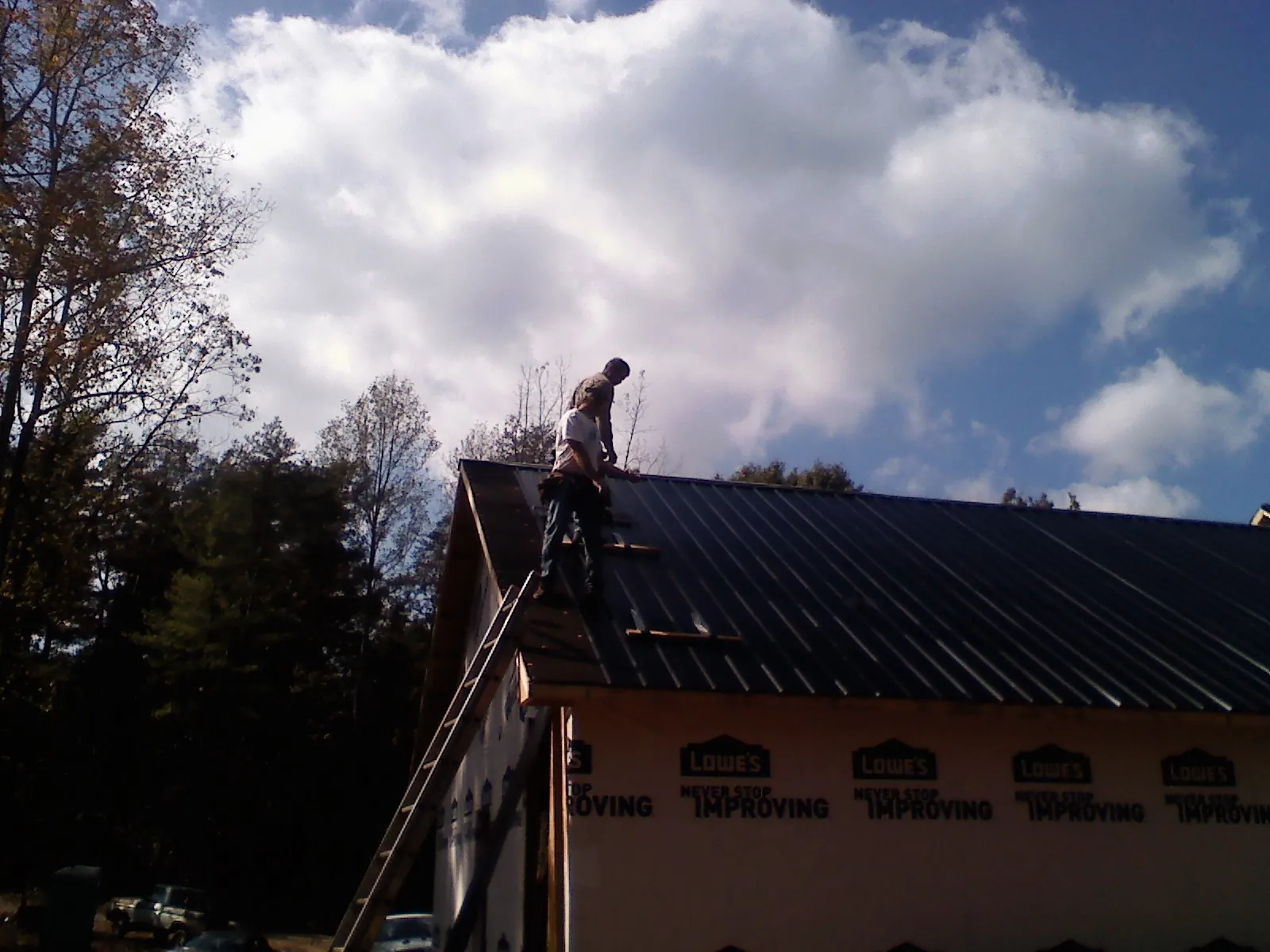 Roofer fastening dark metal panels high against a cloudy sky, from a Roof Inspection job in New Bloomfield